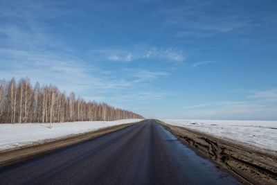 Empty road along snow covered landscape against sky