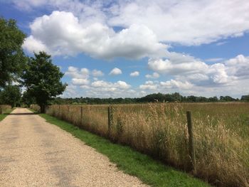 Road passing through field against cloudy sky