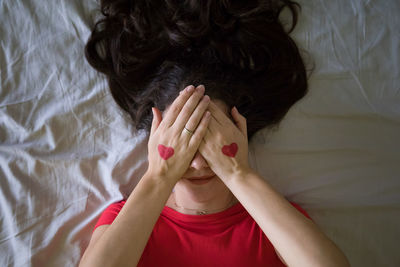 High angle view of young woman with heart shape on hands lying at bedroom