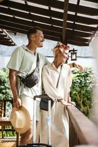 Smiling man with arm around woman standing on porch of villa during vacation