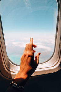 Cropped image of hand on window against sky