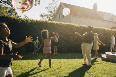 Woman and children playing with balloons in backyard on sunny day