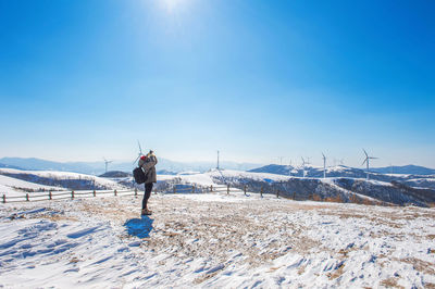 Full length of person photographing through camera while standing on snow covered landscape against blue sky