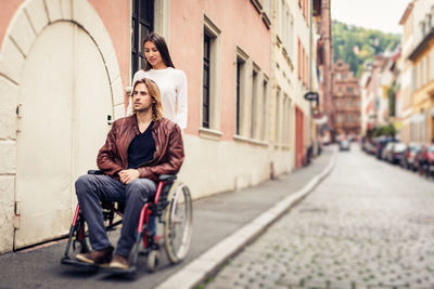 Full length of woman sitting on sidewalk in city