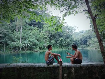 Men sitting by lake against trees