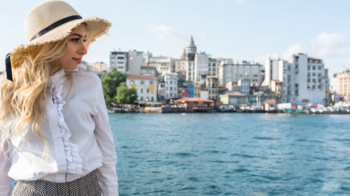 Beautiful woman looking away while standing by river in city