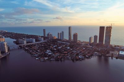 Aerial view of city by sea against sky during sunset