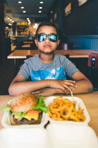Portrait of boy with sunglasses eating fast food at restaurant