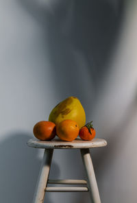 Still life of citrus fruits on white wooden stool against white wall with sunlight and shadow