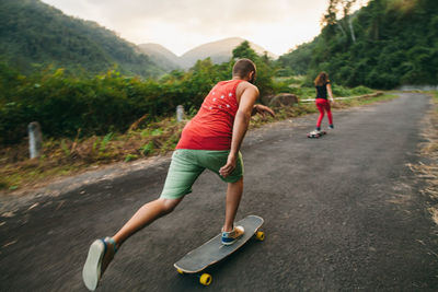 Rear view of people skateboarding on road against mountains