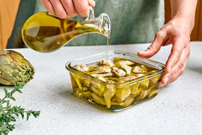 Artichoke hearts marinated with olive oil and herbs.woman pouring oil in jar with pickled artichokes