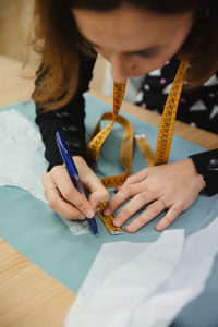 Adult lady using tape to measure garment part on table during work in professional dressmaking workshop