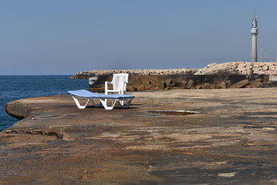 Deck chairs on rocks by sea against clear sky