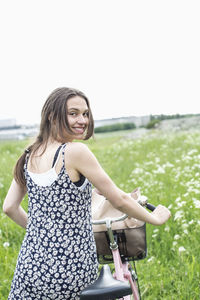 Rear view portrait of young woman standing with bicycle at field