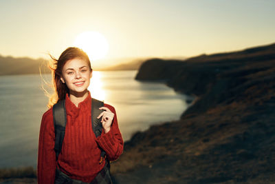 Portrait of smiling young woman standing at beach during sunset