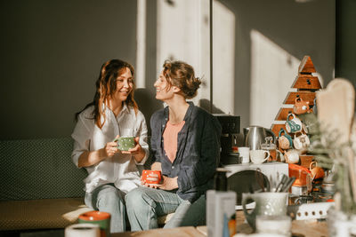 Two female friends enjoying morning coffee in cozy home kitchen