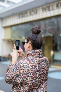 Rear view of woman photographing with mobile phone while standing in city