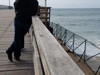 Low section of man standing on pier at sea