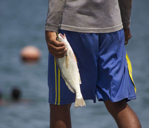 Midsection of man holding fish against sea