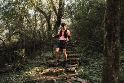 Man traveler with trekking poles walking up old stone stairs in jungles