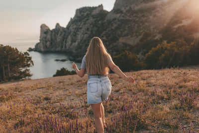 A young girl runs towards the mountains, the sea and the sunset