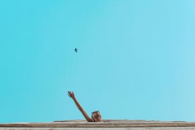 Woman reaching bird against clear blue sky