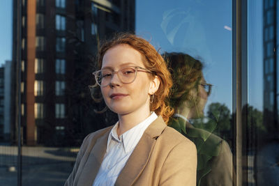 Smiling beautiful young businesswoman leaning on glass wall