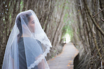 Young woman wearing veil while standing amidst trees