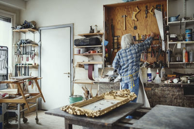 Rear view of senior owner using tools while working at workshop