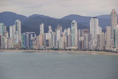 Sea by buildings in city against sky