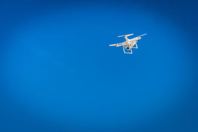 Low angle view of drone flying against clear blue sky during sunny day