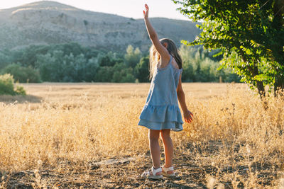 Side view of girl with arms outstretched standing on grassy field against mountain
