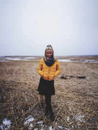 Full length of woman with hands in pockets standing on hay against sky during winter