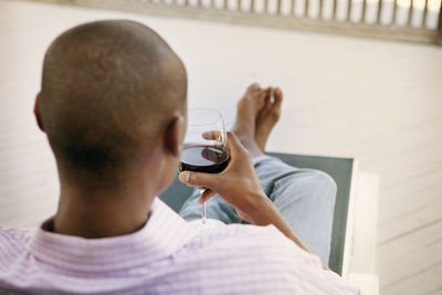 High angle view of man holding wineglass while sitting on deck chair