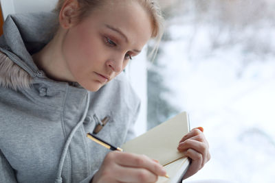 Thoughtful woman writing in diary by window at home