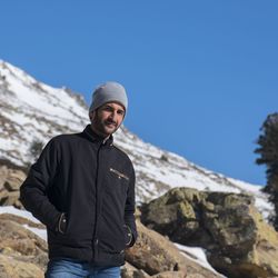 Portrait of young man standing on rock against clear blue sky