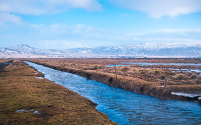 Scenic view of river by snowcapped mountains against sky