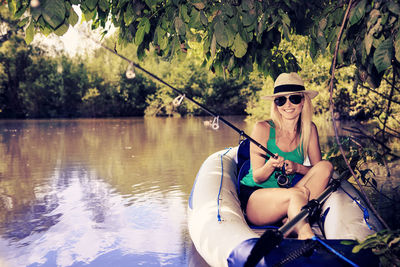 Woman wearing sunglasses fishing while sitting in boat at lake