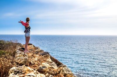 Woman standing on rock by sea against sky