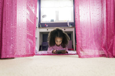 Girl using tablet computer while lying on rug at home