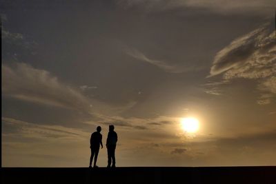 Silhouette friends standing against sky during sunset