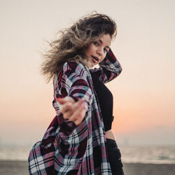 Portrait of young woman standing against sea during sunset