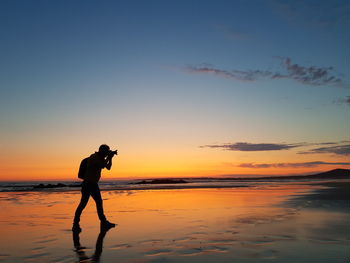 Silhouette man photographing sea against sky during sunset