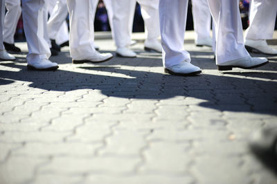 Low section of people wearing white pants and shoes walking on street in city