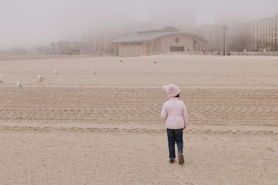 Young girl is playing on an empty beach during a foggy, cold day