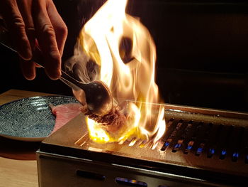 Close-up of cropped hand preparing food on fire