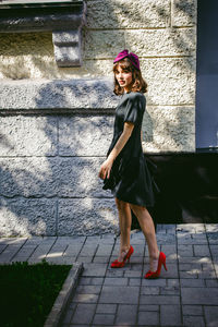 Beautiful young woman in black dress standing by building