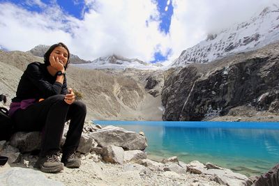 Smiling young woman with hand on chin sitting at lakeshore during winter