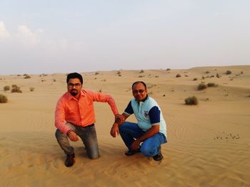 Portrait of friends crouching on desert against sky