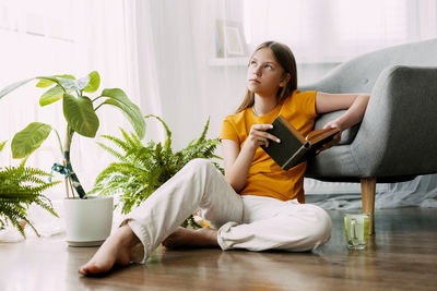 Side view of woman using mobile phone while sitting on sofa at home